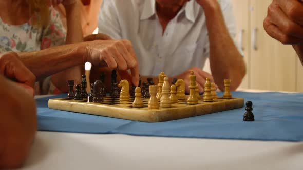 Mid section of senior friends playing chess