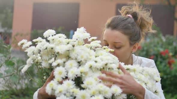 Pretty Young Girl Is Standing Near a Bush of White Chrysanthemums in Park During Spring Time