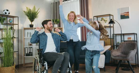 Disabled Man in Wheelchair Watching How Dancing His Cheerful Lovely Wife and Cute 10-Aged Daughter