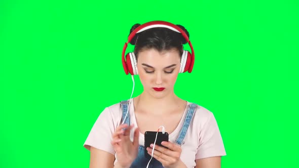 Girl in Big Red Headphones Chooses Music on Mobile Phone on Green Screen, Slow Motion