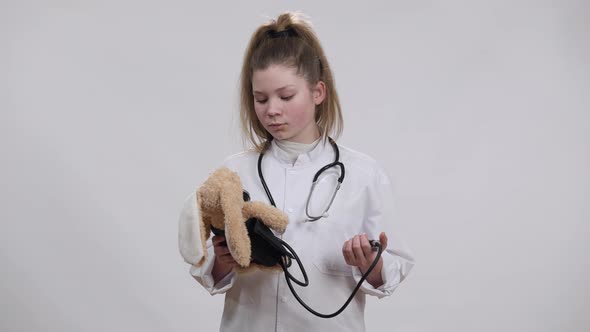 Focused Caucasian Girl in Nurse Gown Measuring Toy Blood Pressure with Sphygmomanometer and Looking