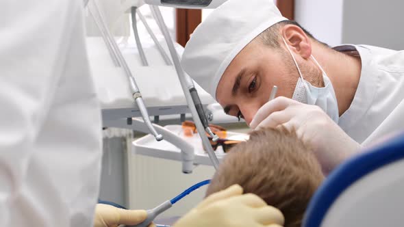 Confident Male Dentist in Uniform Treating Teeth to Child Boy