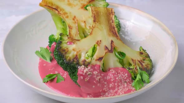 Grilled Broccoli Steak with Pink Beetroot Sauce and Hemp Seeds in White Bowl Plate is Rotating