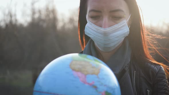 Sad Woman in Medical Mask Holding the Globe at Sunset. COVID-19 Concept.