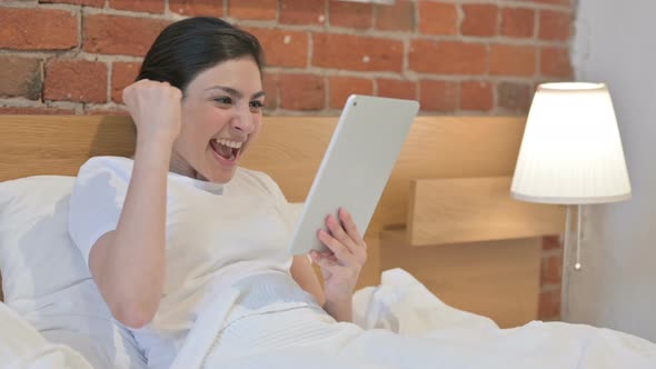 Young Indian Woman Celebrating Success on Tablet in Bed