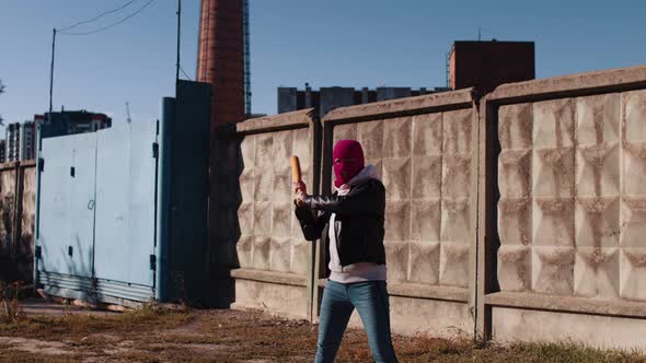 Young woman in pink balaclava with baseball bat in hands.