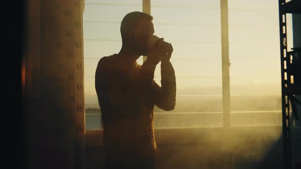 Silhouette of boy drinks tea at the window