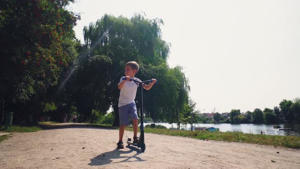 A Boy Rides a Scooter in a City Park