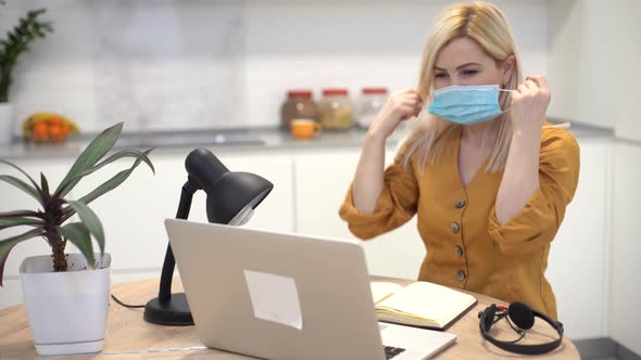 Woman in Protective Mask Works Remotely on Laptop at Home in the Kitchen Woman Takes Off Mask