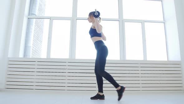 Home Fitness Concept. Young Woman with a Barbell Does Exercises in a White Interior