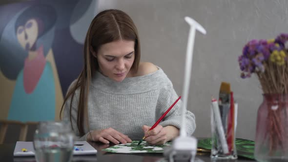 Portrait of Charming Attractive Caucasian Woman Painting Sitting at Table Looking Out the Window