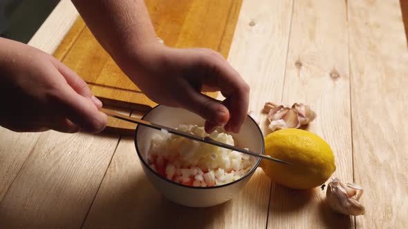 A woman's hands use a knife to transfer sliced onions from a cutting board to a bowl of sliced