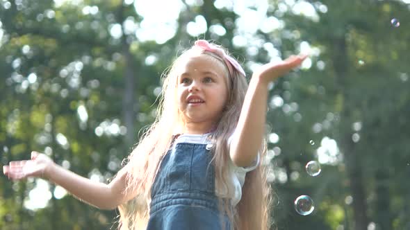 Little happy child girl cathing and bursting soap bubbles outdoors in summer.