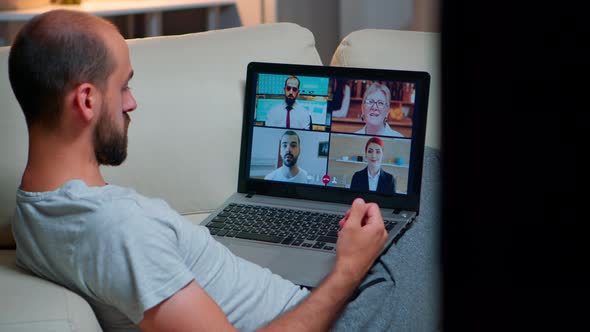 Over Shoulder View of Man in Pajamas Having Online Conversation with Teammates