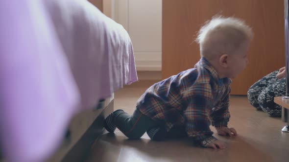 Baby Crawls to Rack Near Young Mother in Children Room