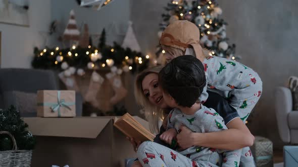 Young Family with Two Small Children Reading a Book for Christmas Happy Woman with Sons on Winter