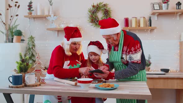 Senior Grandparents and Grandchild Watching Cooking Lesson Using Digital Tablet at Christmas Kitchen