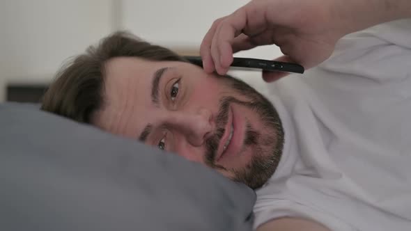 Portrait of Young Man Talking on Call on Smartphone in Bed