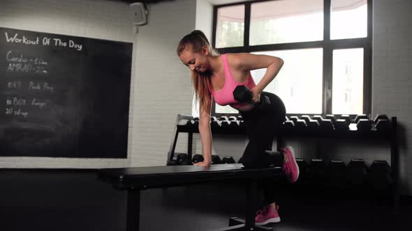 Athletic girl athlete trains her back with dumbbells in the gym. Dumbbell bench press