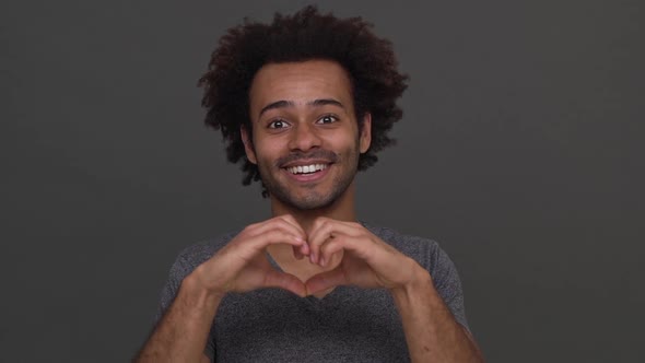 Dark Skinned Cool Man Making Heart with Hands Enjoying Time Isolated on Charcoal Background