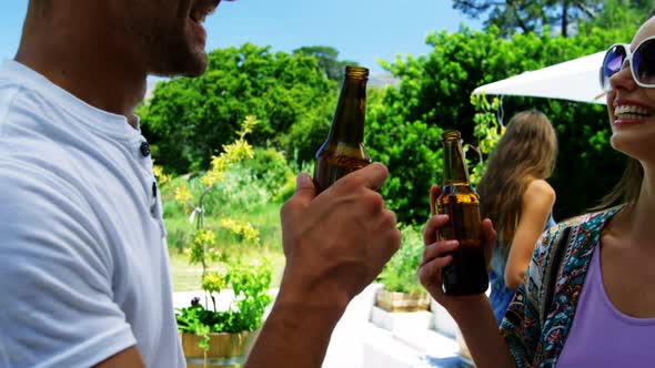 Couple interacting while having a bottle of beer near poolside