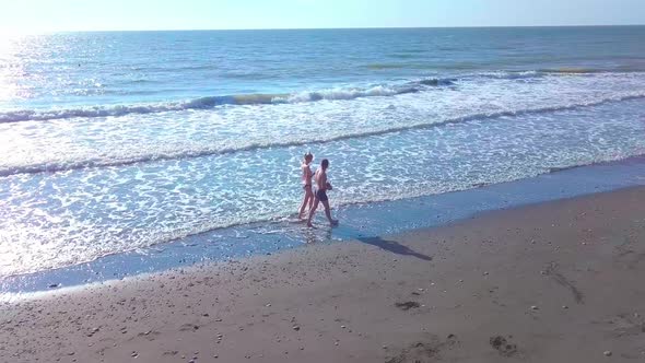 A guy and a woman are walking along a deserted beach, in the surf.