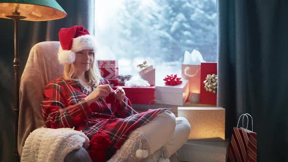 Relaxed Young Woman Knitting Red Scarf with Needles in Cozy Mountain Cabin