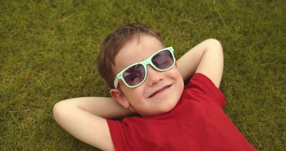 Happy Cute Little Boy Lies on the Green Grass a Child in Sunglasses Lies on the Grass Resting