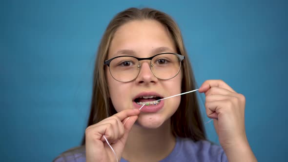 Girl with Braces Brushing Your Teeth with Dental Floss. A Girl with Colored Braces on Her Teeth