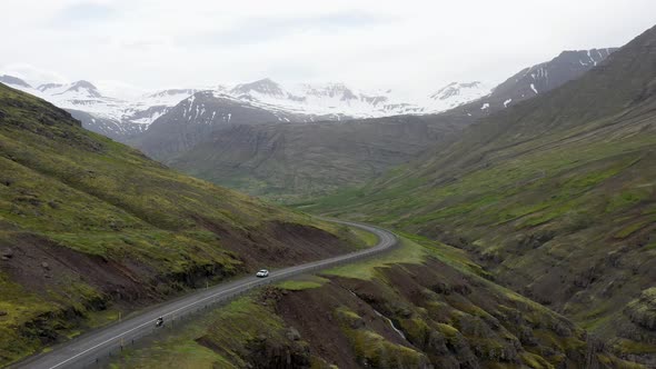 Motorcycle passing car in the mountains of Iceland with drone video moving back.