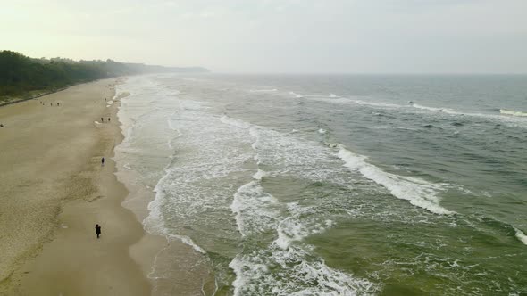 Aerial flyover south coast of the Baltic Sea in  Wladyslawowo, Poland, the foamy sea in Autumn, peop