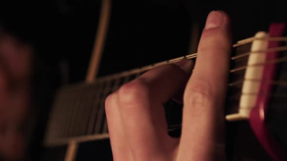 Man Playing Acoustic Guitar at Home in Atmospheric Dark Warm Lighting