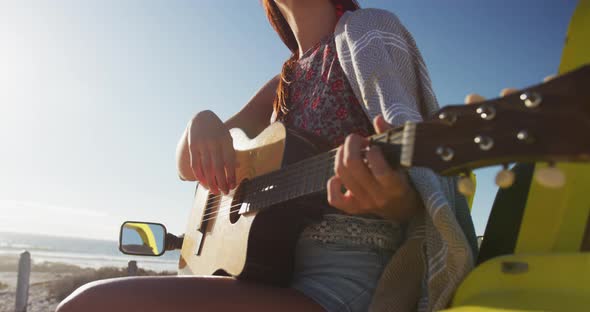 Happy caucasian woman sitting in beach buggy by the sea playing guitar