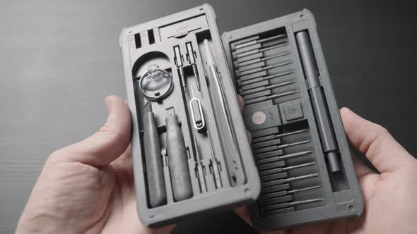 Set of Screwdrivers with Gray Handles in a Box in Male Hands on a Dark Table Background