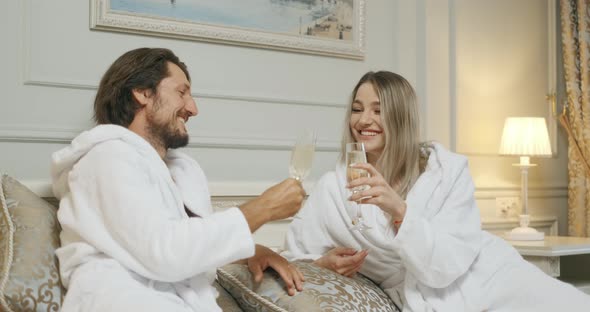 Affectionate Couple Toasting with Champagne Lying on Their Bed. Hotel, Travel, Relationships and