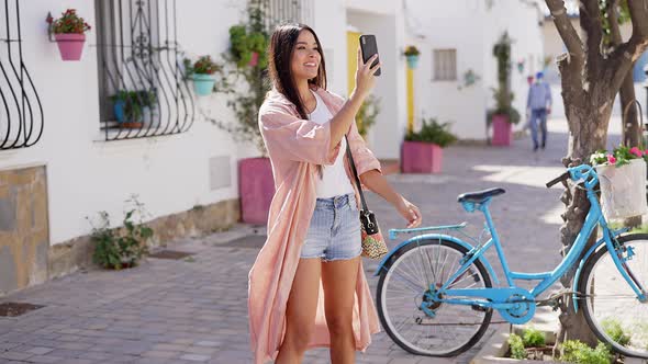 Cheerful Hispanic Woman Using Smartphone on Street