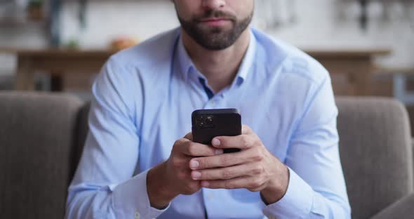 Portrait Shot of the Cheerful Young Man Taping While Texting on the Smartphone Device in the Living