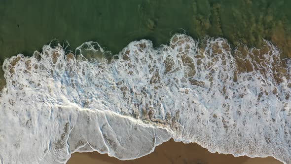 A drone reveals crystal clear water and crashing waves on a beautifully sunny California coast.