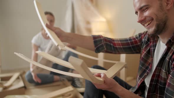 Young Adults Moving in New Home. Couple Moving in Assembling Chair Furniture. Young Interracial