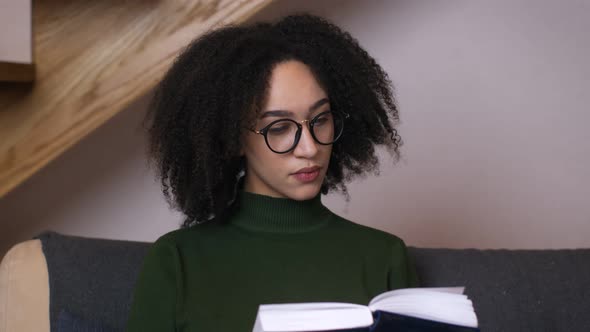 Young African American Woman in Eyeglasses Reading Book at Home Interior Close Up Slow Motion