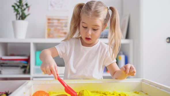 Little blonde girl with two ponytales play with magic sand