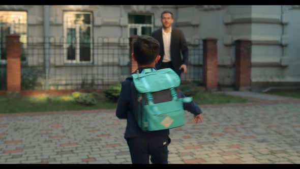 Backside View of Boy with Bag Wearing Uniform Running Into Father embrace.Happy Dad in Suit Waiting