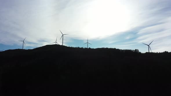 Silhouette of wind turbines against bright sky with dark mountain foreground - 5 rotating turbines a