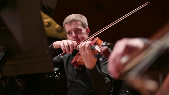 Young male violinist playing the violin to the accompaniment of the orchestra