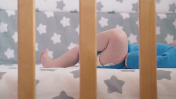 Small Baby Kicks Legs Lying in New Cot with Stylish Textile