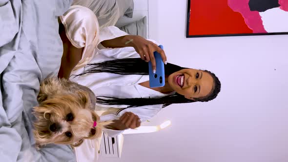 A Cute African American Woman Sits on Her Bed Petting Her Yorkshire Terrier Dog and Looks at Her