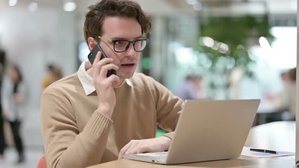 Man Talking on Smartphone While Working on Laptop