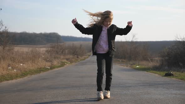 Cheerful Female Child with Long Blonde Hair Dances Funny on the Road at Countryside