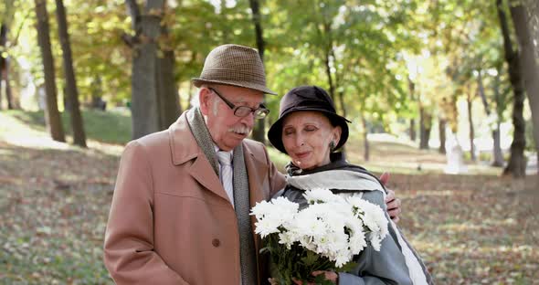 Portrait of Happy Retired Couple in Love with Bouquet of Flowers Talk and Smile