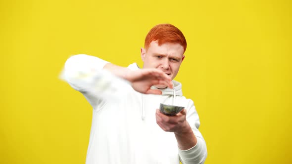 Wealthy Millennial Redhead Man Scattering Money in Slow Motion at Yellow Background